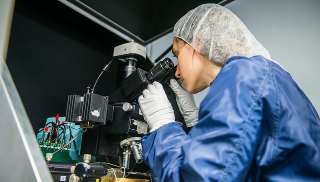 Gwénaëlle qui regarde à travers un microscope habillé dans la combinaison pour les salles blanches