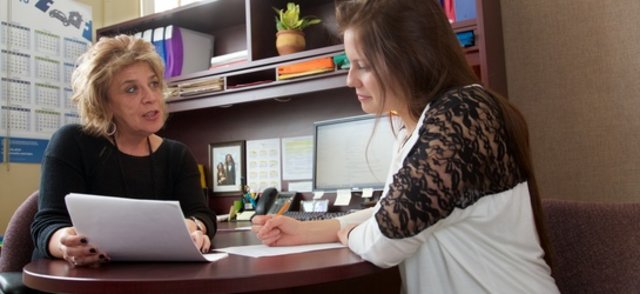 À son bureau, une professionnelle travaille sur des documents avec une étudiante.