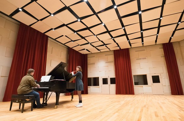 Une personne au piano à queue et une à la flûte traversière dans une salle avec plancher de bois franc et plafond de panneaux acoustiques