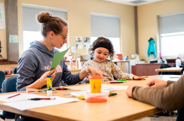 Personne étudiante et une enfant assises autour d’une table lors d’une intervention en ergothérapie.