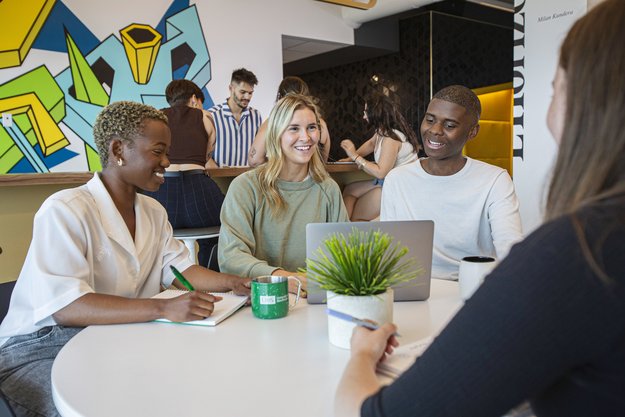 Personnes étudiantes installées autour d'une table poruv travailler en équipe. Au fond, une murale dynamique.