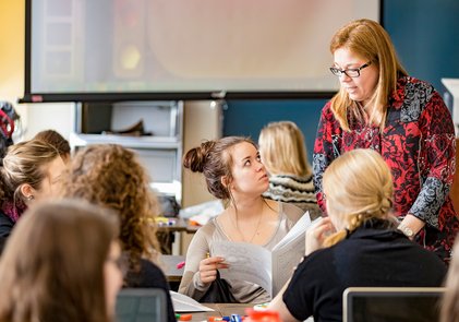 une professeure discute avec une étudiante parmi un groupe installé autour d'une table.