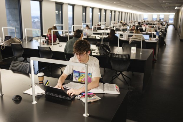Étudiant travaillant à l'ordinateur à table dans une bibliothèque ultra moderne.