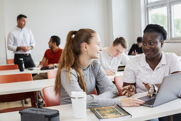 Étudiantes et étudiants en discussion dans une salle de classe avec grandes tables de type auditorium