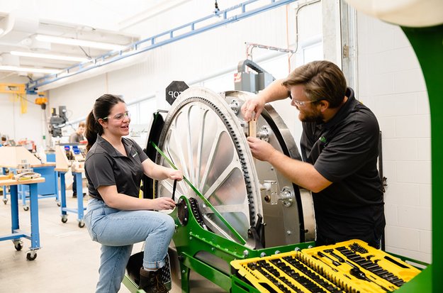 Un étudiant et une étudiante dans un laboratoire de génie robotique travaillant sur de la machinerie agricole. 