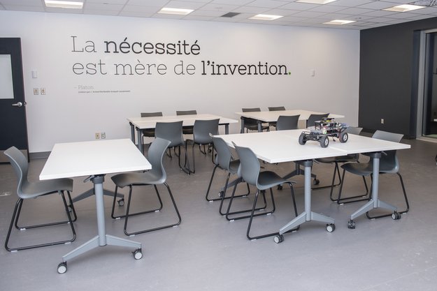 Espace épuré avec tables de travail et, au mur, la citation La nécessité est mère de l'invention.