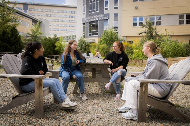 Quatre étudiantes assises dans des chaises Adirondak avec le pavillon en arrière-plan