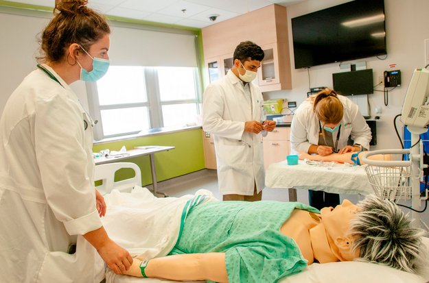 Personnes étudiantes et enseignantes dans un laboratoire de simulation clinique avec un mannequin et un bras model.