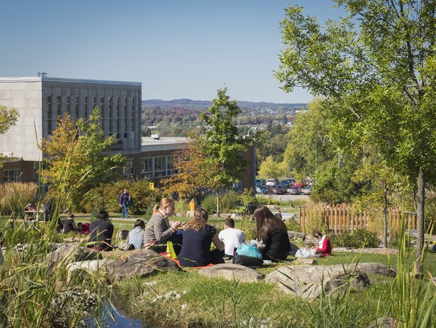 Personnes étudiantes assises au sol avec vue vers un pavillon et le mont Orford au loin