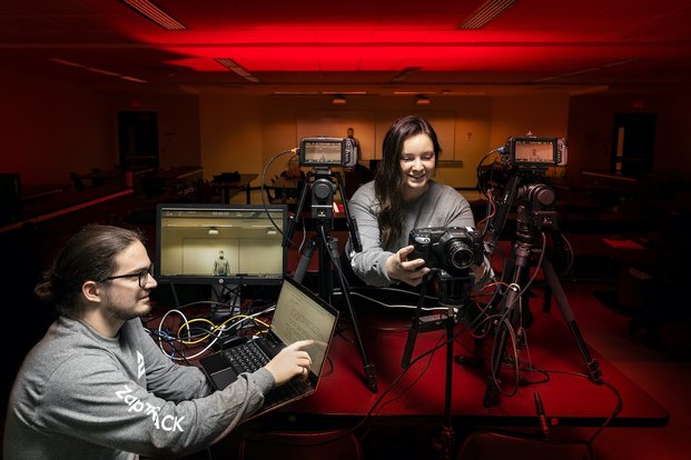Dans une salle éclairée en rouge, deux personnes étudiants travaillent en commun avec un ordinateur et un appareil photo.