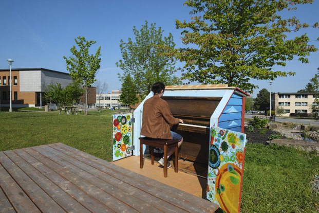 Homme jouant sur un piano entouré de panneau peints de motifs colorés, en plein air