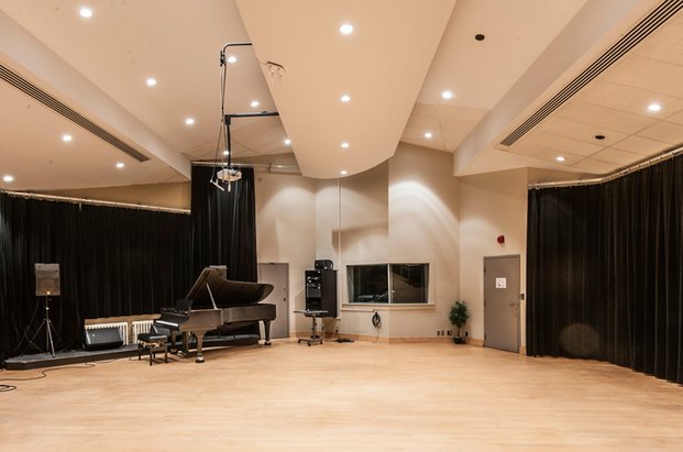 Grand piano à queue dans une salle avec plafond multiniveaux, plancher de bois, rideaux noirs et fenêtre de salle d'écoute.