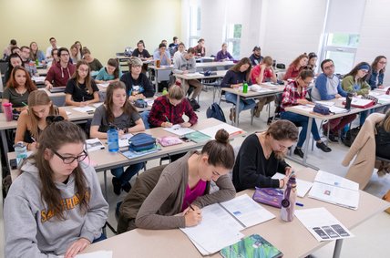 Salle de classe remplie de personnes étudiantes travaillant dans leurs cahiers.