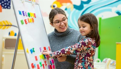 Petite élève qui place des aimants sur un tableau avec une enseignante accroupie à côté qui l'observe..