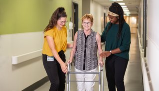 2 étudiantes en ergothérapie qui aident une vieille dame à marcher