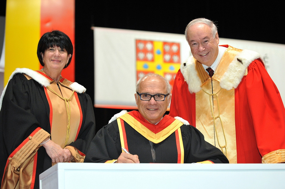 Le professeur Grand'Maison signe un registre, entouré de la secrétaire générale Monique Richer et du recteur Denis Brière de l'Université Laval.